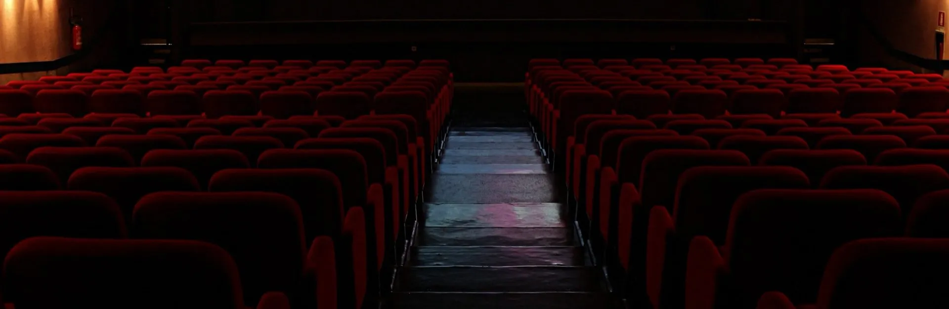 La platea del Cinema Apollo in penombra: file di poltrone rosse e la scalinata centrale